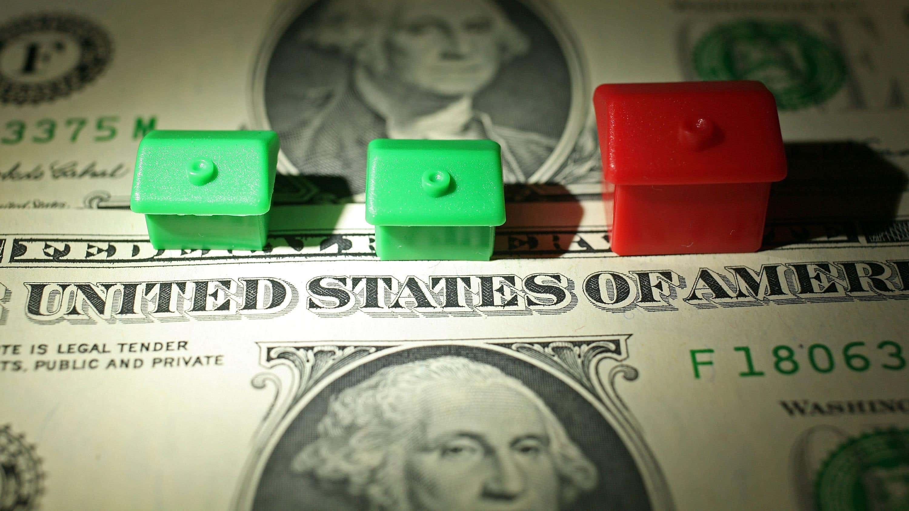 منزلان احتكاريان باللون الأخضر وواحد باللون الأحمر فوق ورقتين نقديتين بقيمة دولار واحد